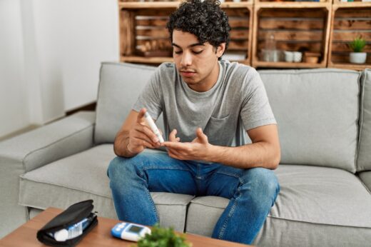 Young,hispanic,diabetic,man,measuring,glucose,sitting,on,the,sofa