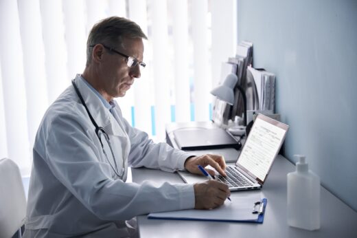 Serious,mature,old,doctor,physician,making,medical,notes,in,notebook